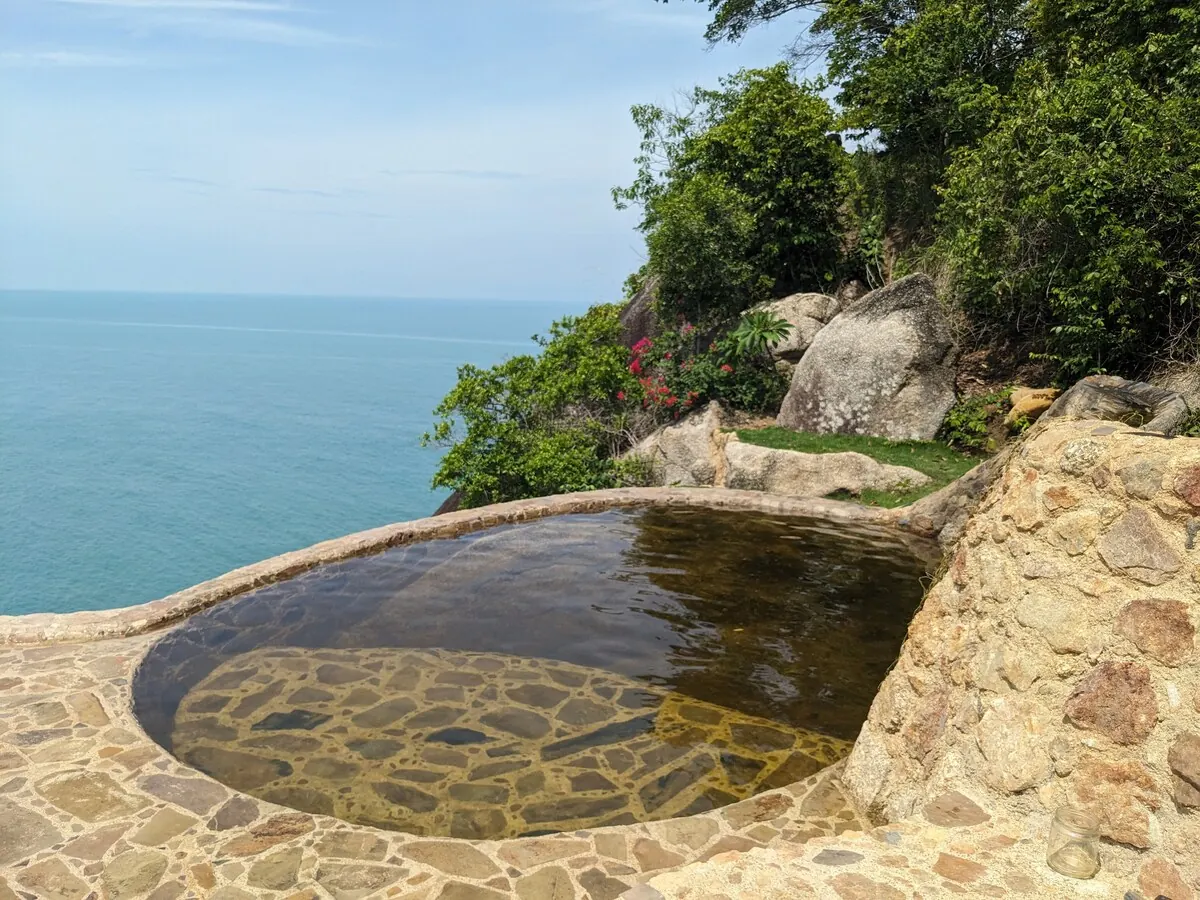 Natural stone pool set into the rock with sea and jungle beyond