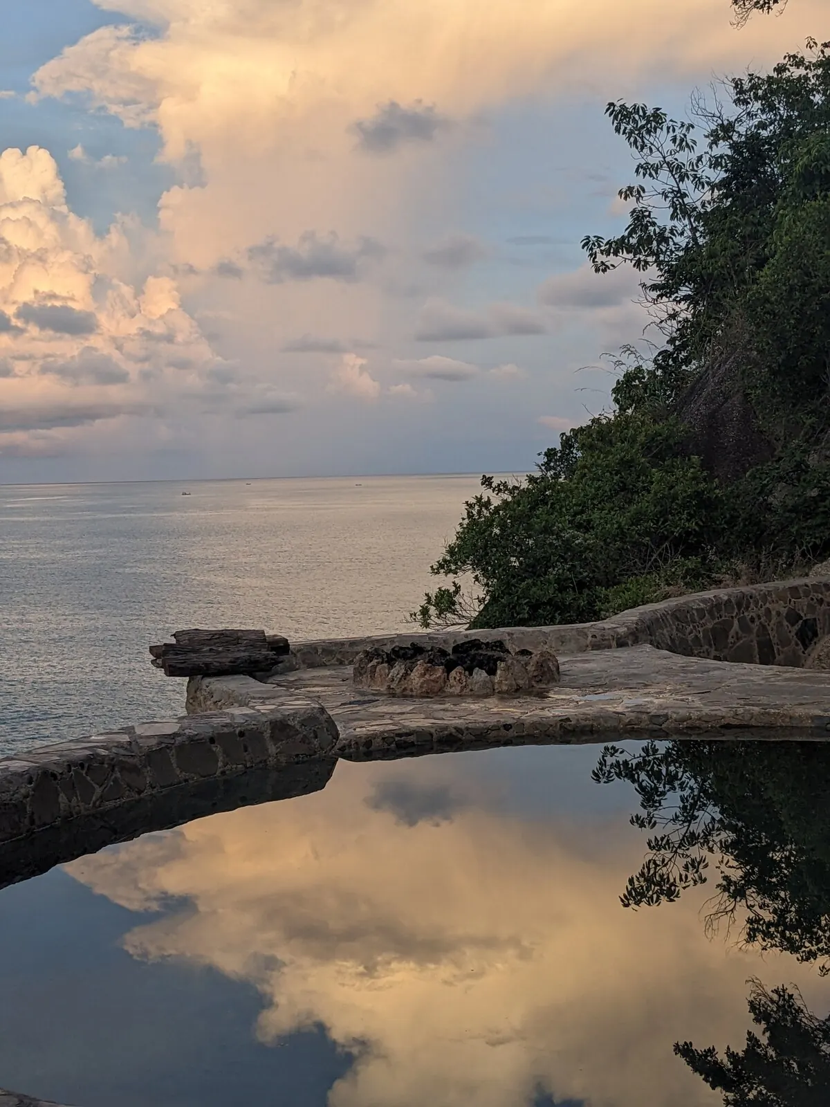 Pool surface reflecting a pastel sunset sky over the sea